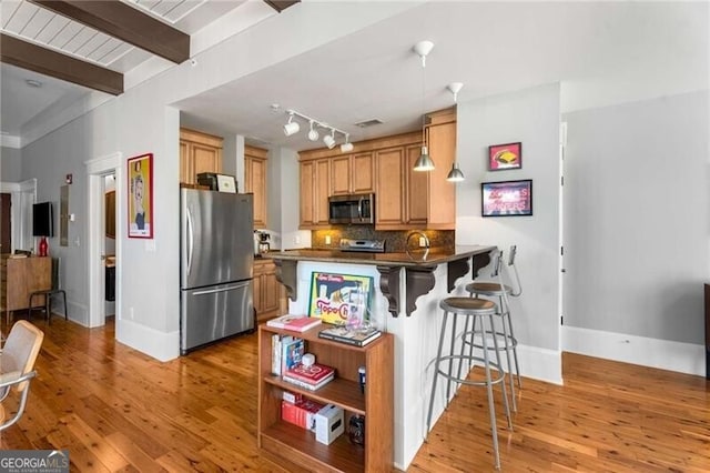 kitchen featuring light hardwood / wood-style flooring, appliances with stainless steel finishes, backsplash, a kitchen breakfast bar, and kitchen peninsula