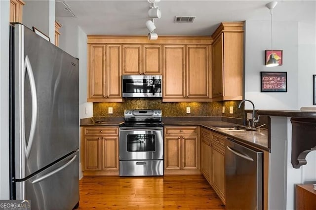 kitchen with decorative light fixtures, tasteful backsplash, sink, stainless steel appliances, and light wood-type flooring