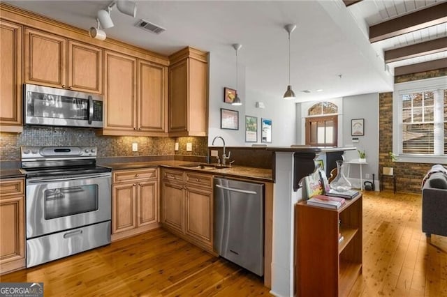 kitchen featuring pendant lighting, sink, appliances with stainless steel finishes, decorative backsplash, and kitchen peninsula