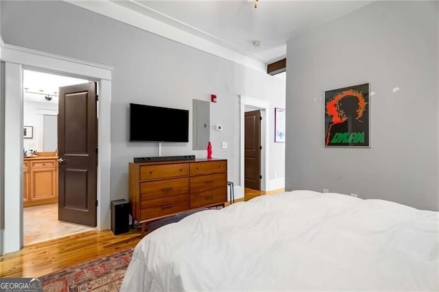 bedroom featuring beamed ceiling, connected bathroom, and light hardwood / wood-style flooring