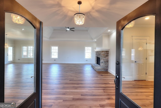 unfurnished living room with a stone fireplace, hardwood / wood-style floors, ornamental molding, ceiling fan, and a tray ceiling