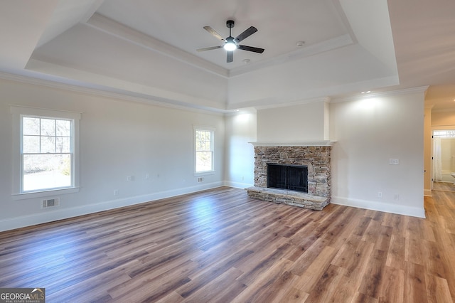 unfurnished living room with crown molding, wood-type flooring, a raised ceiling, ceiling fan, and a fireplace