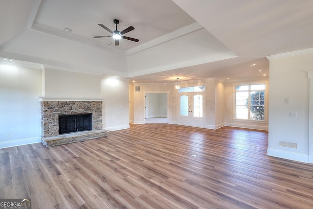 unfurnished living room featuring ornamental molding, a tray ceiling, ceiling fan, a fireplace, and hardwood / wood-style floors