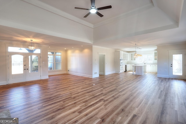 unfurnished living room with hardwood / wood-style flooring, ornamental molding, ceiling fan with notable chandelier, and french doors