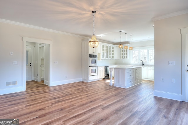 kitchen featuring a kitchen island, double oven, white cabinets, light hardwood / wood-style floors, and crown molding