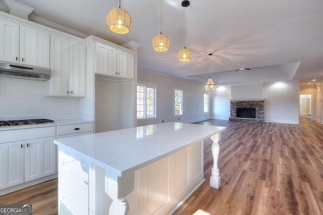 kitchen with a stone fireplace, white cabinetry, gas cooktop, pendant lighting, and light stone countertops