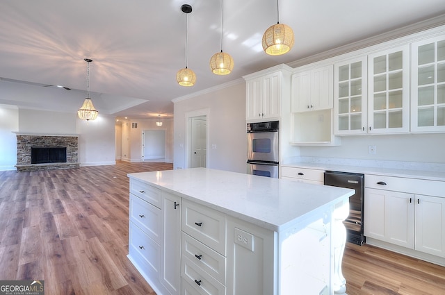 kitchen featuring hanging light fixtures, double oven, a kitchen island, light stone countertops, and white cabinets