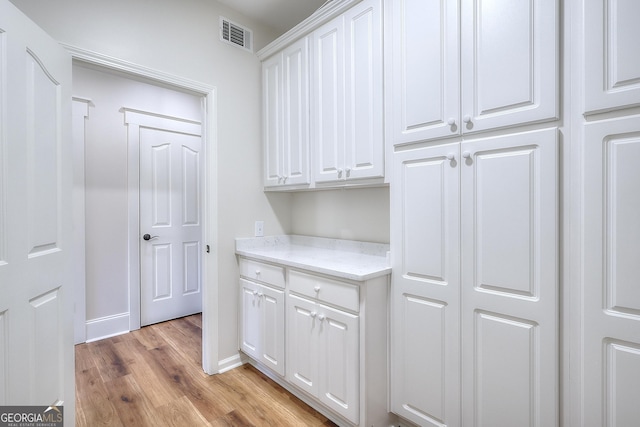 kitchen with light stone counters, light hardwood / wood-style flooring, and white cabinets