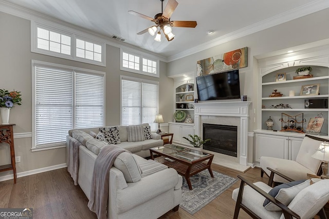 living room with built in shelves, a healthy amount of sunlight, ornamental molding, and hardwood / wood-style floors