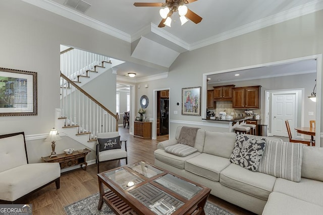 living room with hardwood / wood-style floors, crown molding, ceiling fan, and a towering ceiling