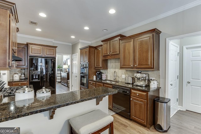 kitchen featuring sink, a breakfast bar area, black appliances, dark stone counters, and light wood-type flooring