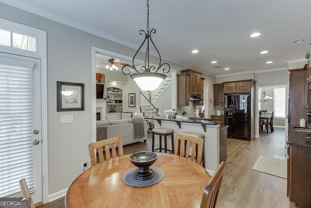 dining room with crown molding, built in features, ceiling fan, and light wood-type flooring