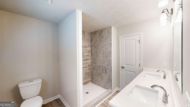 bathroom with vanity, a textured ceiling, toilet, and tiled shower