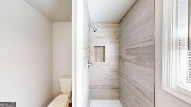 bathroom with a tile shower and toilet