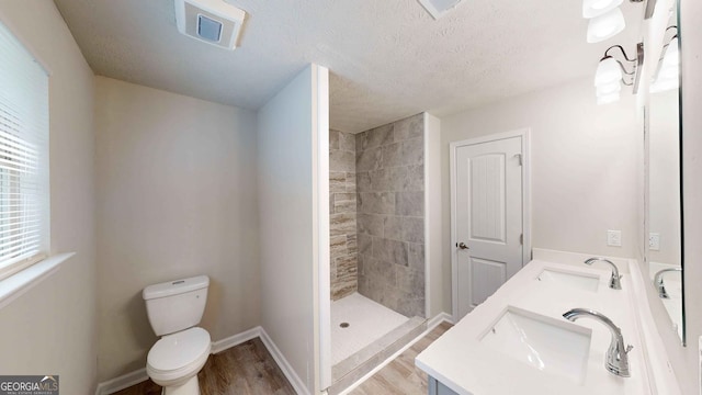 bathroom featuring hardwood / wood-style floors, a tile shower, vanity, a textured ceiling, and toilet