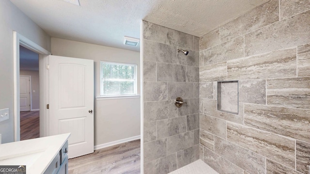 bathroom featuring tiled shower, vanity, wood-type flooring, and a textured ceiling