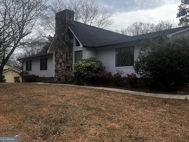 view of home's exterior with a shingled roof, a chimney, and a lawn