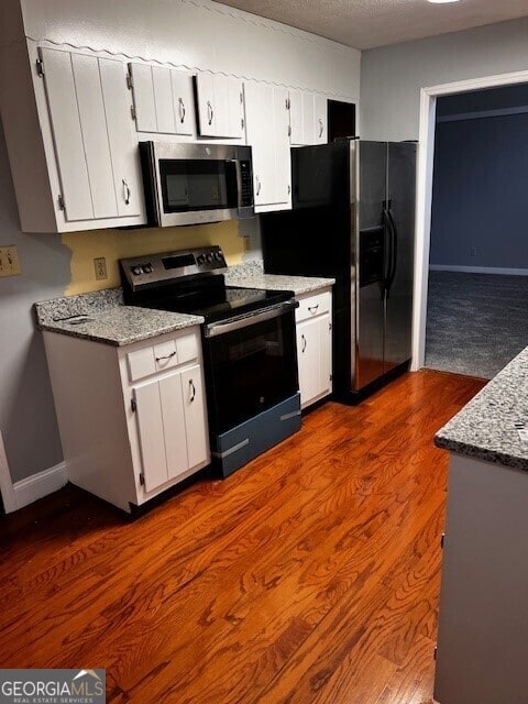 kitchen with dark wood-type flooring, appliances with stainless steel finishes, light stone counters, and white cabinets