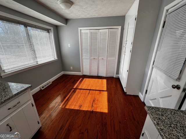 unfurnished bedroom with a textured ceiling, dark wood-type flooring, visible vents, baseboards, and a closet