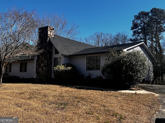 view of property exterior featuring a yard, a shingled roof, a chimney, and driveway