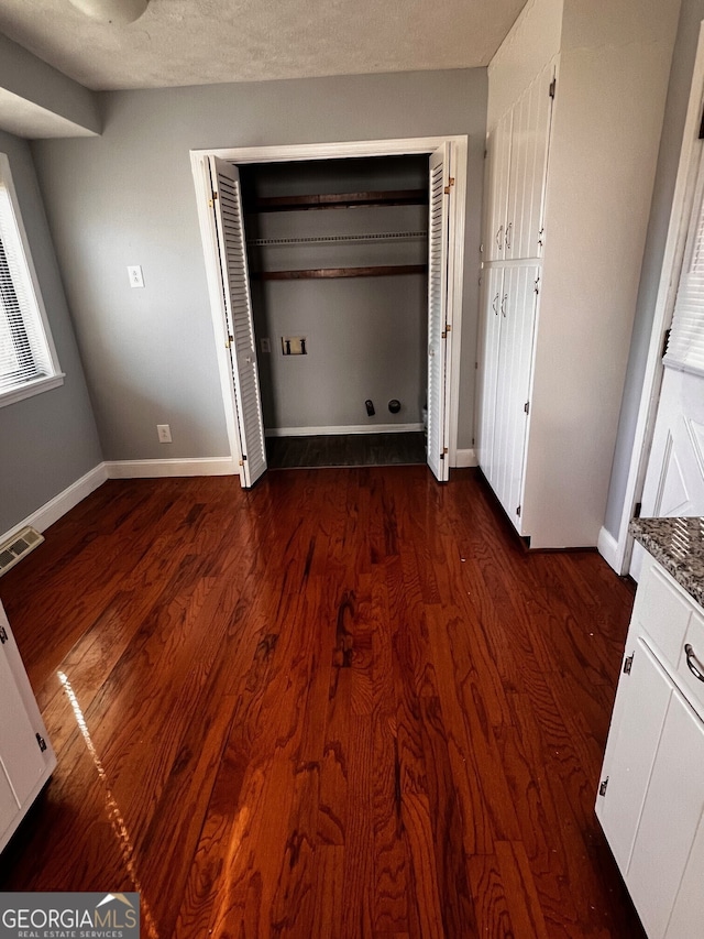 unfurnished bedroom with dark wood-style floors, a textured ceiling, visible vents, and baseboards