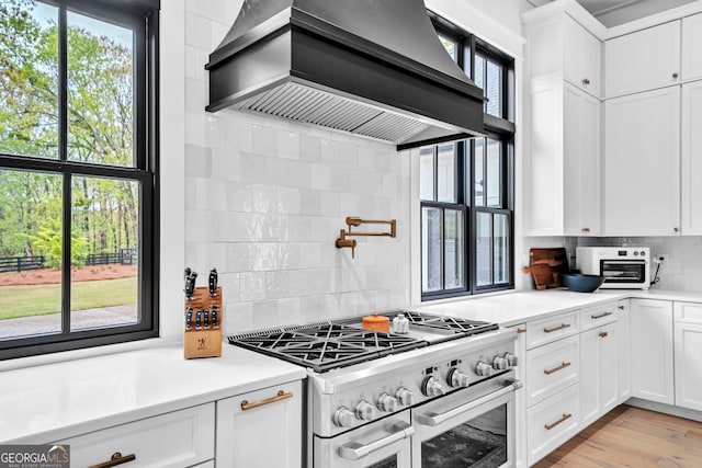 kitchen with a wealth of natural light, stainless steel stove, custom range hood, and white cabinets