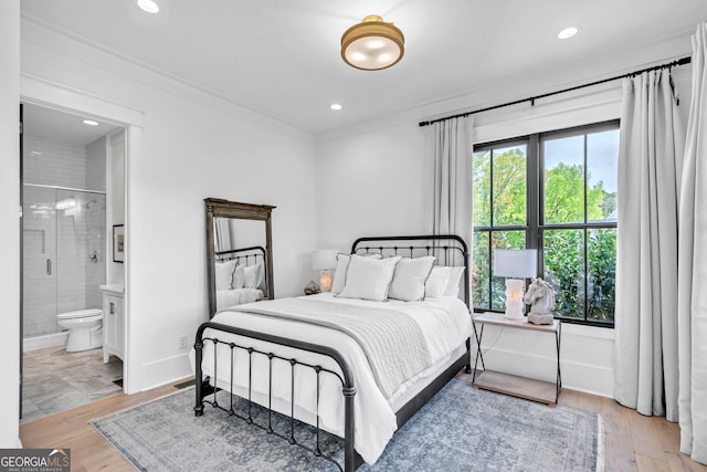 bedroom featuring ornamental molding, ensuite bath, and light hardwood / wood-style flooring