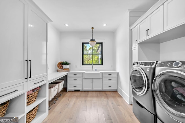 laundry room featuring washer and dryer, sink, cabinets, and light hardwood / wood-style floors