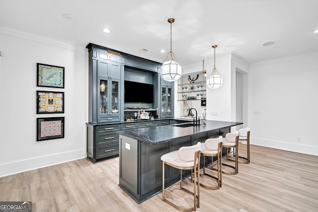 kitchen featuring sink, a breakfast bar area, hanging light fixtures, ornamental molding, and dark stone counters