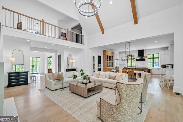 living room with a towering ceiling, light hardwood / wood-style floors, a chandelier, and beamed ceiling