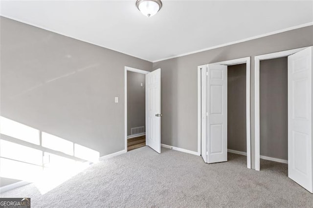 unfurnished bedroom with multiple closets, crown molding, and light carpet