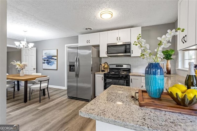 kitchen featuring decorative light fixtures, light hardwood / wood-style flooring, stainless steel appliances, and white cabinets