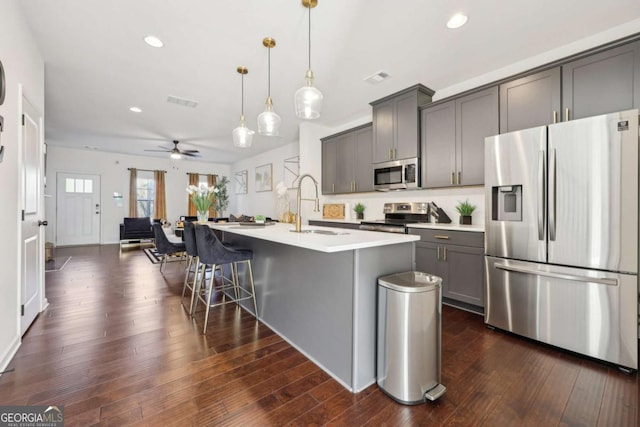 kitchen featuring sink, gray cabinetry, hanging light fixtures, a center island with sink, and stainless steel appliances