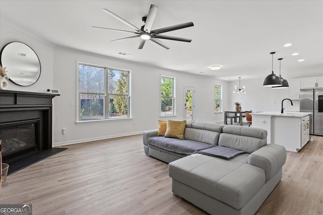 living room featuring ornamental molding, sink, ceiling fan with notable chandelier, and light wood-type flooring