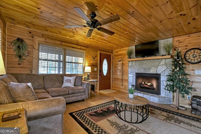 living room featuring a stone fireplace, wood walls, wooden ceiling, light wood-type flooring, and ceiling fan