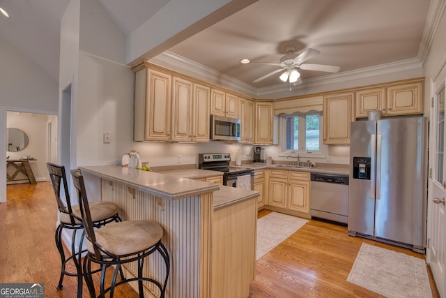 kitchen with sink, a kitchen bar, kitchen peninsula, stainless steel appliances, and light wood-type flooring