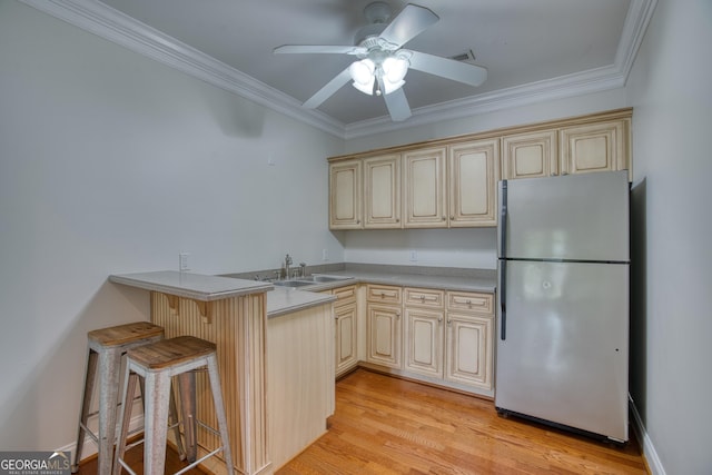 kitchen featuring sink, a breakfast bar area, stainless steel fridge, ornamental molding, and kitchen peninsula