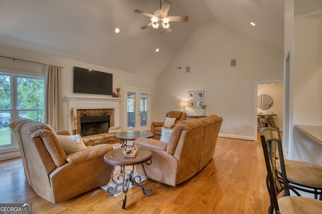 living room featuring ceiling fan, a stone fireplace, high vaulted ceiling, and light wood-type flooring