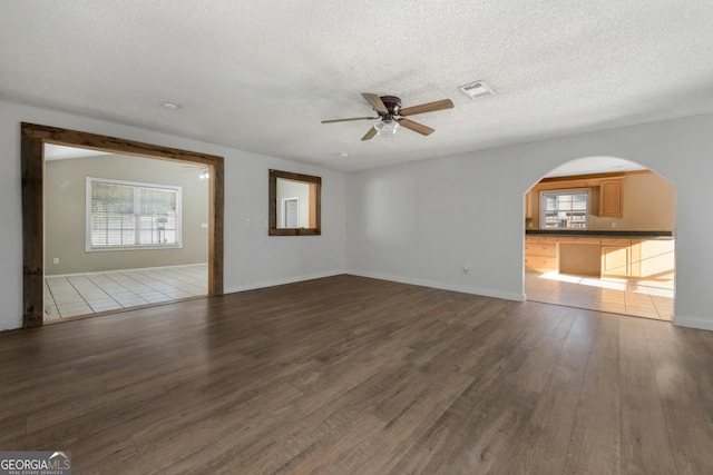 unfurnished living room featuring ceiling fan, dark hardwood / wood-style flooring, and a textured ceiling