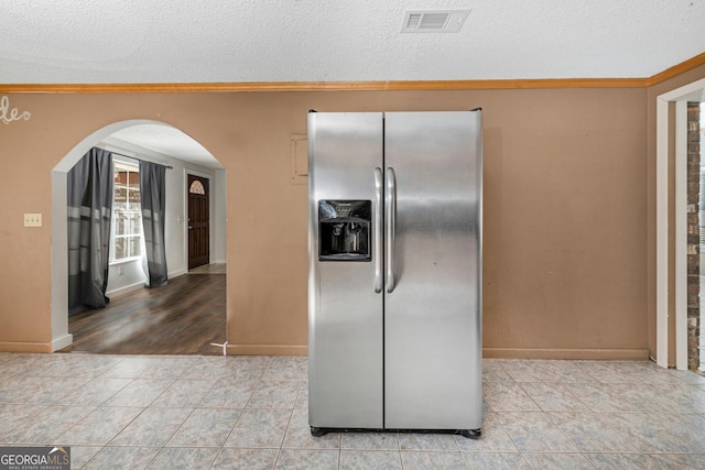 kitchen featuring stainless steel refrigerator with ice dispenser, crown molding, light tile patterned flooring, and a textured ceiling