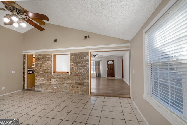 tiled spare room with vaulted ceiling, brick wall, a healthy amount of sunlight, and a textured ceiling