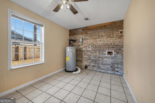 unfurnished room with light tile patterned floors, water heater, ceiling fan, a textured ceiling, and brick wall