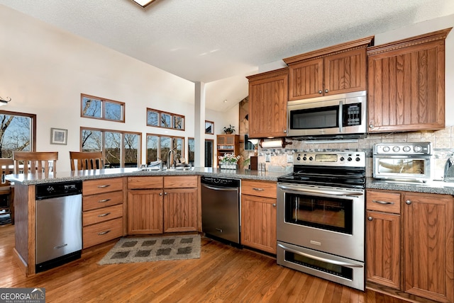 kitchen with decorative backsplash, light hardwood / wood-style floors, kitchen peninsula, and appliances with stainless steel finishes