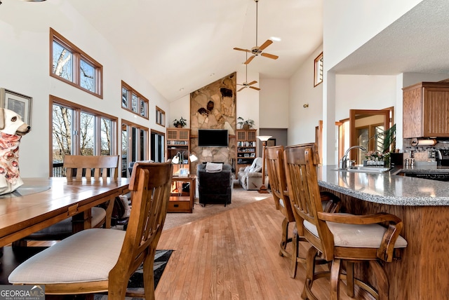 dining room featuring ceiling fan, high vaulted ceiling, sink, and light hardwood / wood-style flooring