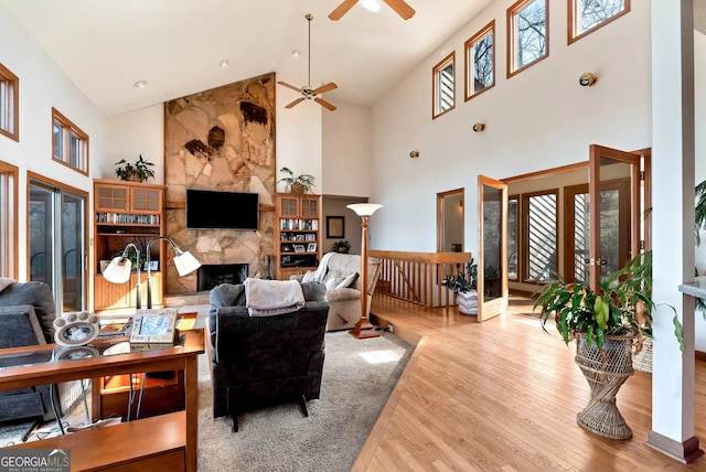 living room featuring ceiling fan, high vaulted ceiling, a fireplace, and light hardwood / wood-style floors