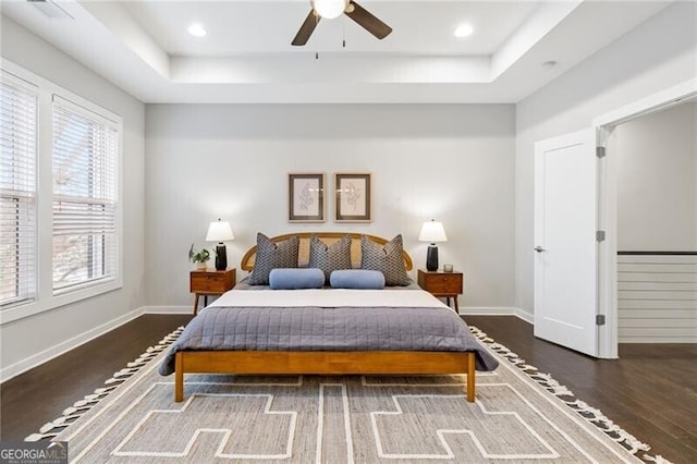 bedroom featuring dark wood-type flooring, a raised ceiling, and ceiling fan