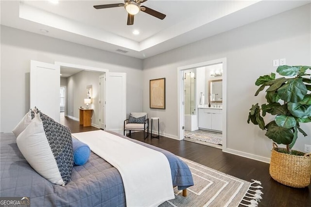 bedroom with dark wood-type flooring, ceiling fan, ensuite bathroom, and a raised ceiling