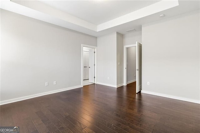 unfurnished room with dark hardwood / wood-style flooring and a tray ceiling