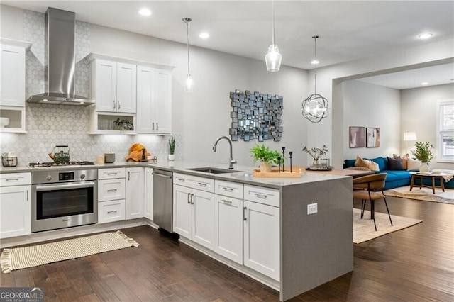 kitchen with appliances with stainless steel finishes, decorative light fixtures, white cabinets, kitchen peninsula, and wall chimney exhaust hood