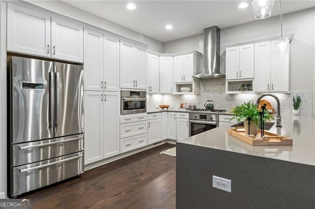 kitchen with wall chimney range hood, decorative light fixtures, white cabinets, and appliances with stainless steel finishes